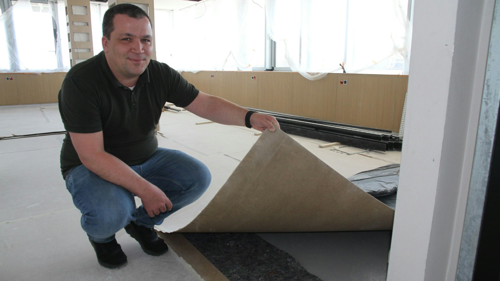Ein Mann hockt auf dem Boden und hält die Schutzabdeckung für einen Bodenbelag in die Höhe.