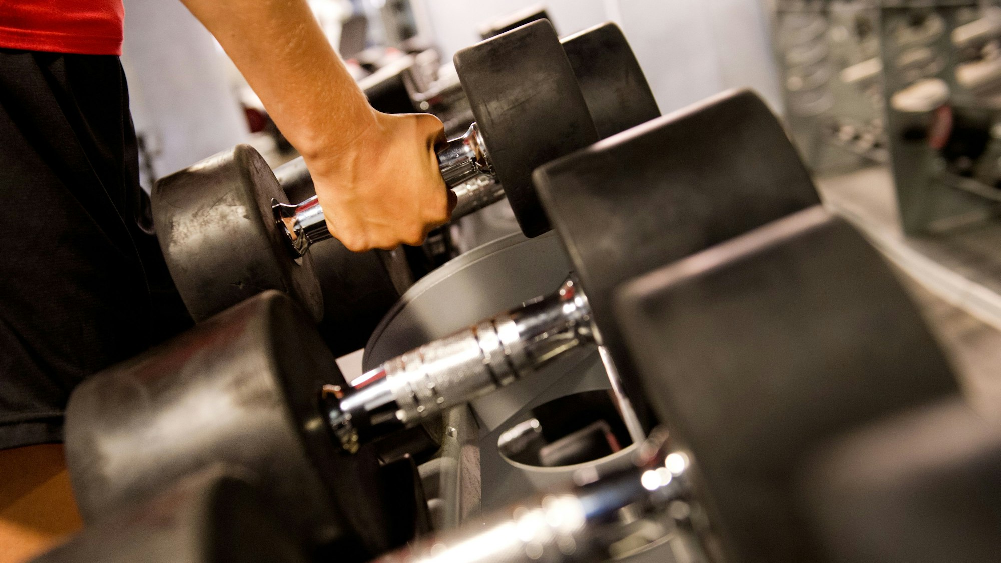 Jemand nimmt eine Hantel von einer Hantelbank