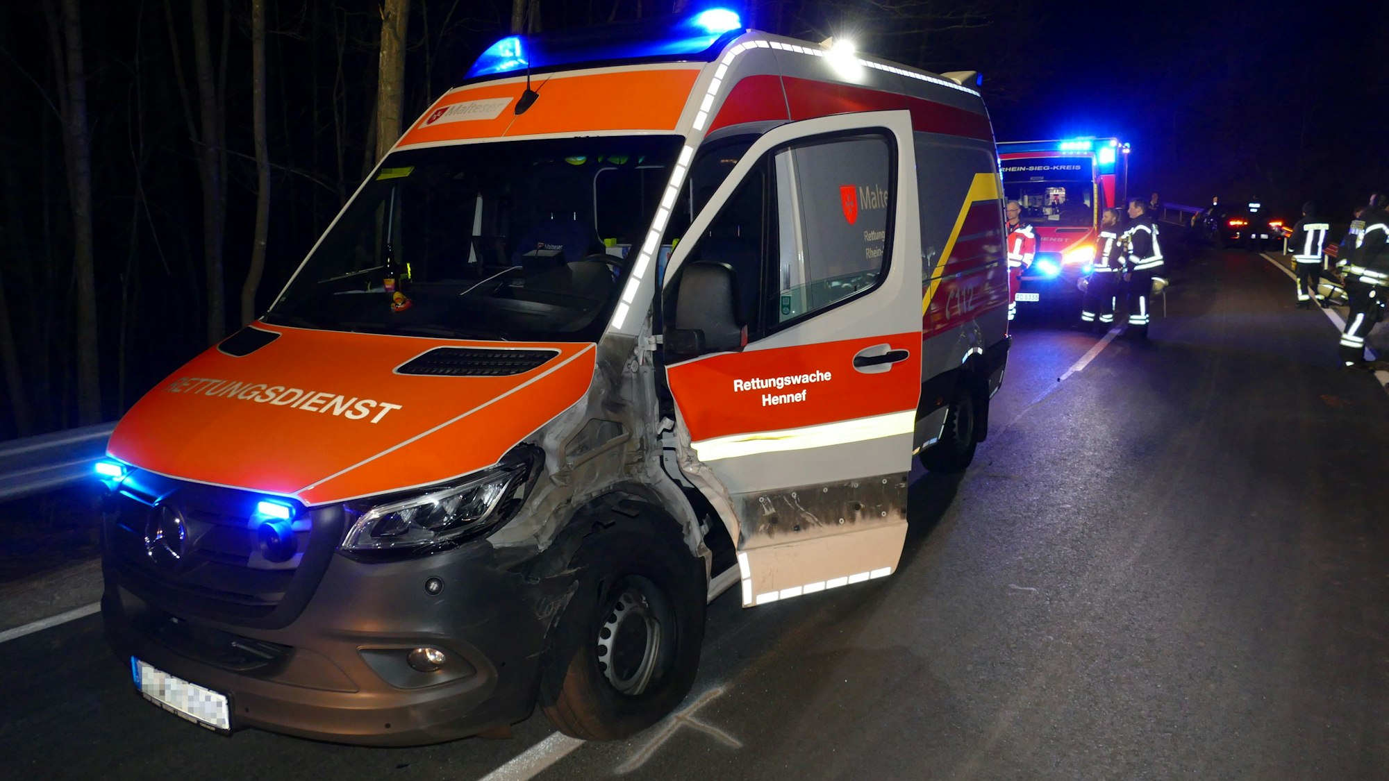 Ein defekter Krankenwagen steht in der Nacht auf einer Straße. Die eine Seite ist nach einem Unfall verbeult, die Tür steht offen.