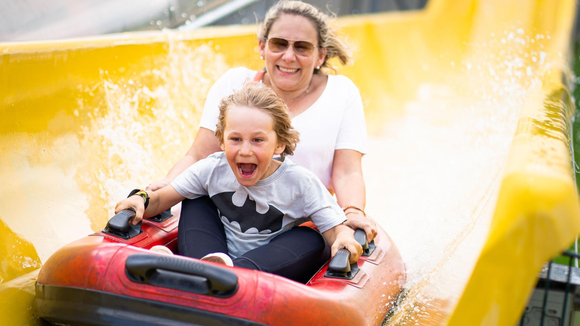 Ein Kind und eine Frau sitzen in einem Bötchen in der Wasserrutsche im Bubenheimer Spieleland.