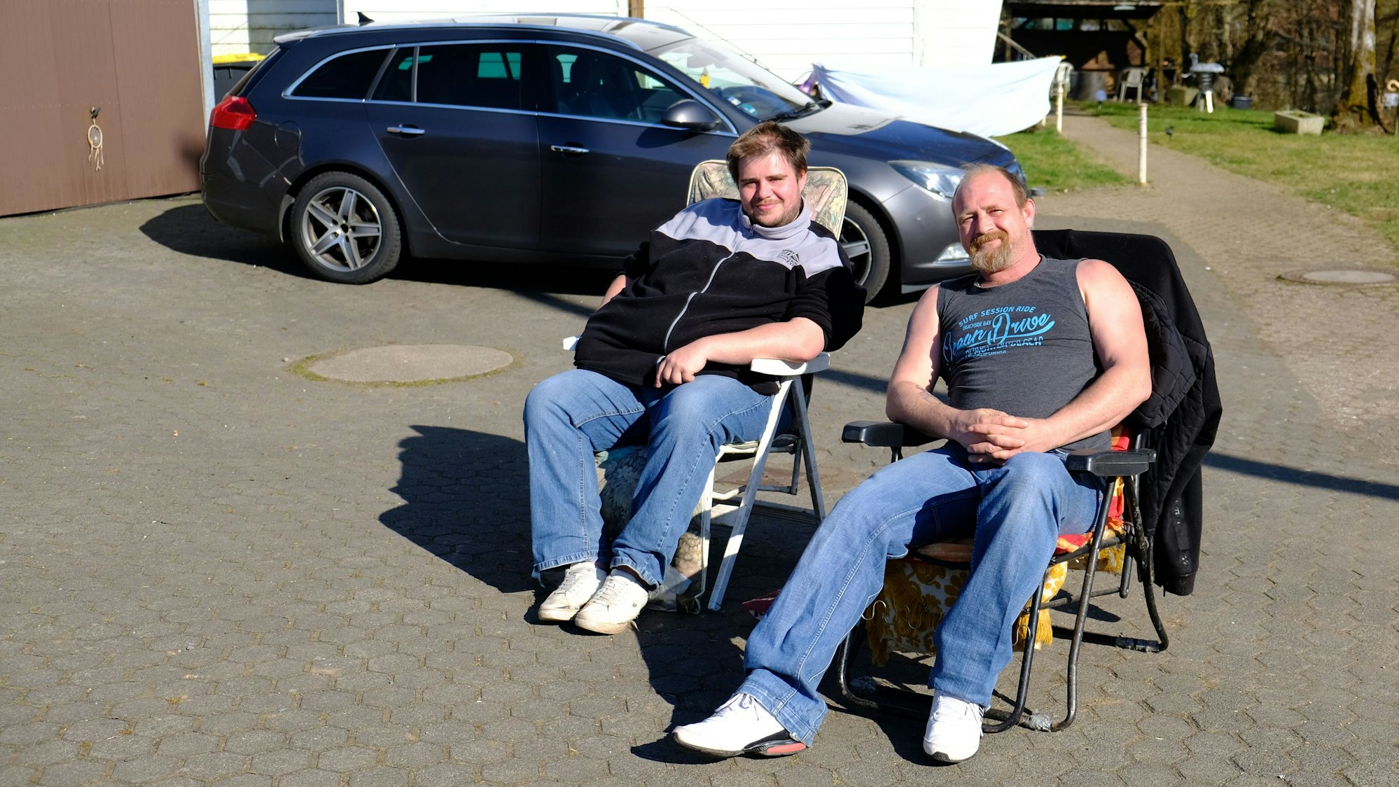 Zwei Anwohner sitzen auf Campingstühlen in der Sonne und beobachten die Polizeiaktion.