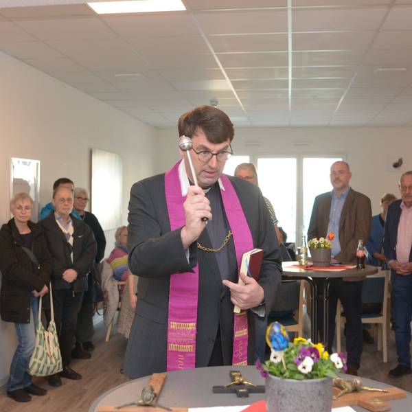 Das Bild zeigt den Priester mit dem Aspergill, die Gäste im Hintergrund schauen ihm zu.