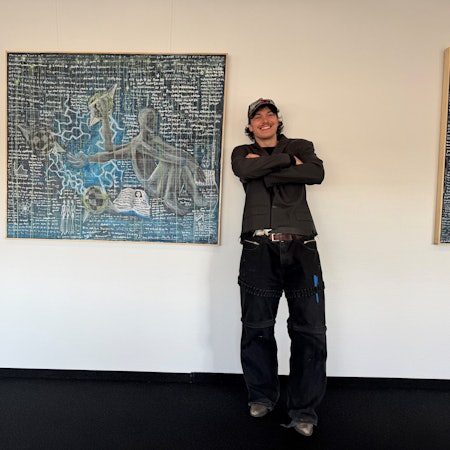 Auf dem Bild ist ein junger Künstler vor einem seiner Werke zu sehen.