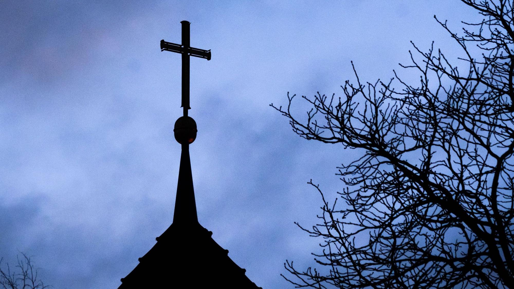 ARCHIV - 25.01.2024, Niedersachsen, Hannover: Dunkle Wolken ziehen über das Kreuz auf einer evangelischen Kirche in der Region Hannover hinweg.
