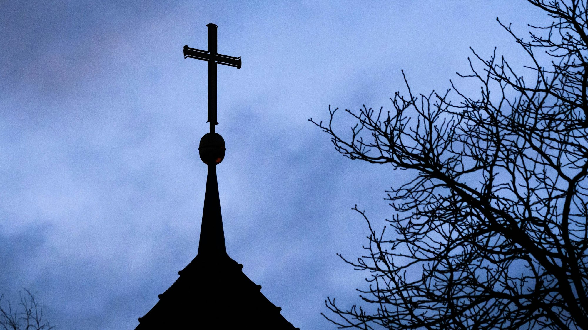 ARCHIV - 25.01.2024, Niedersachsen, Hannover: Dunkle Wolken ziehen über das Kreuz auf einer evangelischen Kirche in der Region Hannover hinweg.