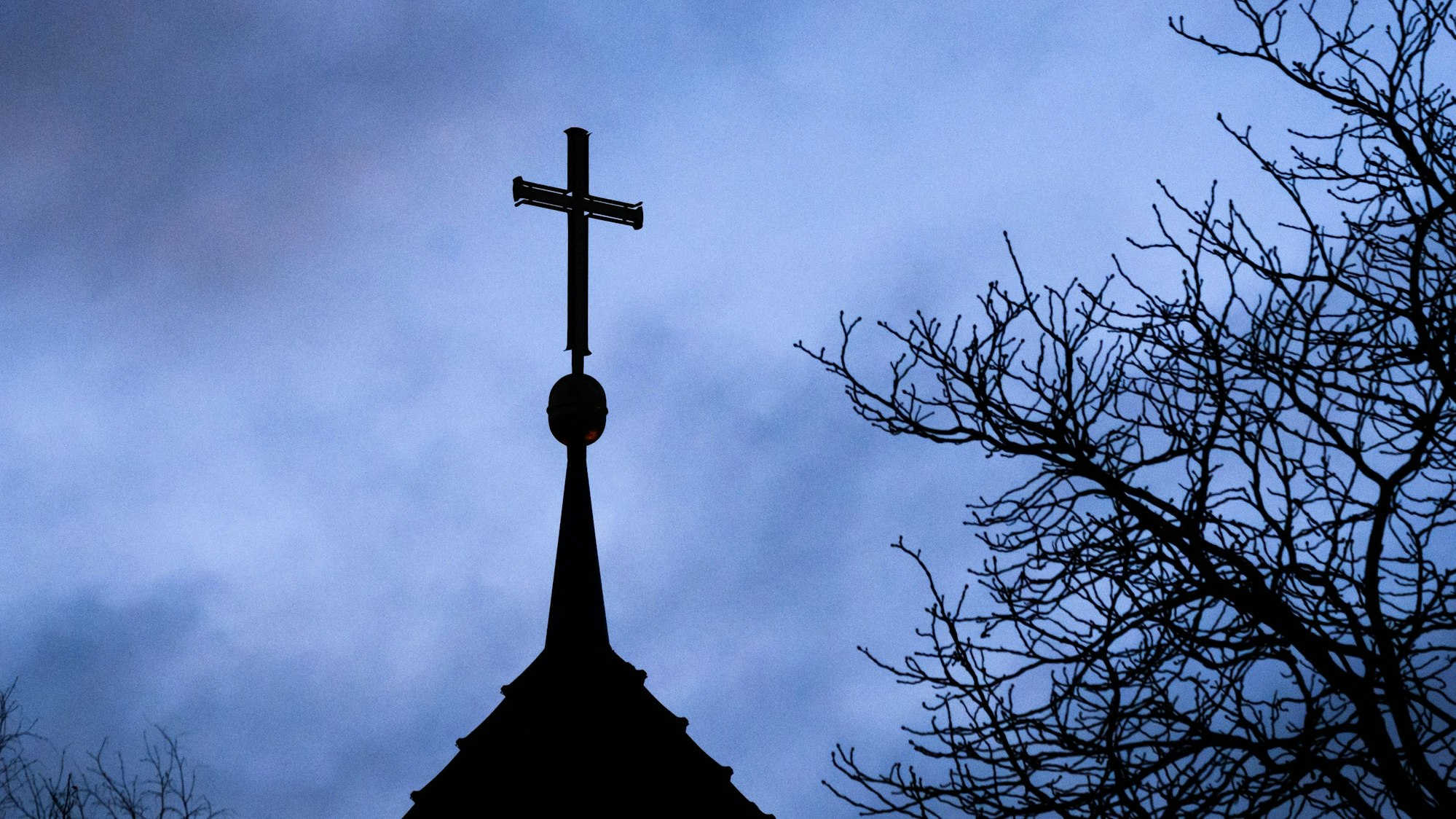 Dunkle Wolken ziehen über das Kreuz auf einer evangelischen Kirche in der Region Hannover hinweg.
