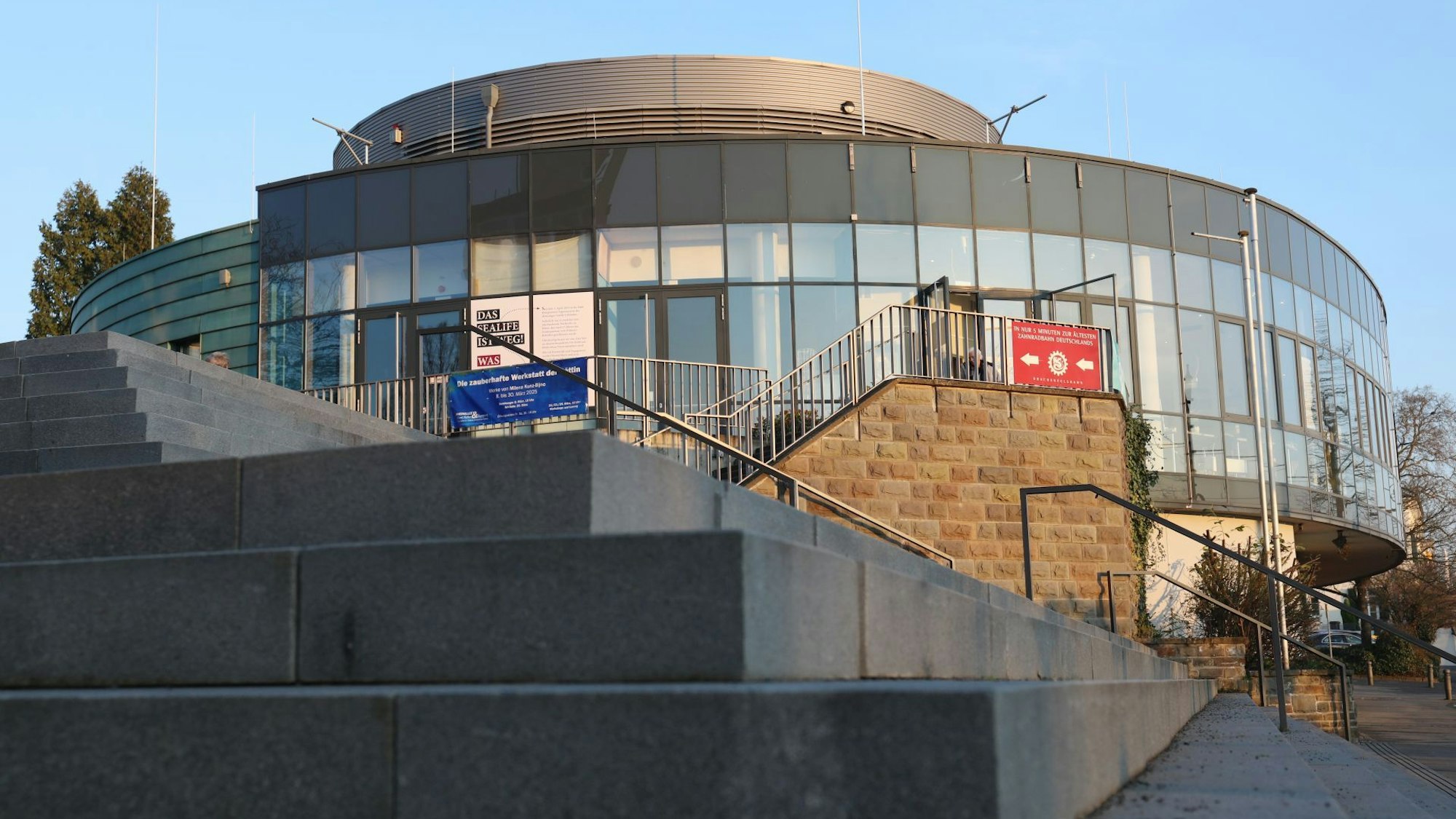 Eine große Treppenanlage und im Hintergrund ein ovales Gebäude mit einer Glasfront.