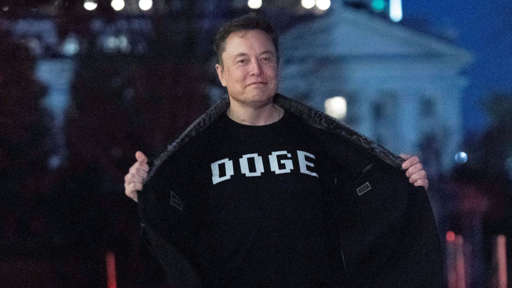 Das Bild zeigt Elon Musk mit einem T-Shirt mit der Aufschrift "DOGE", während er auf dem Südrasen des Weißen Hauses in Washington geht.