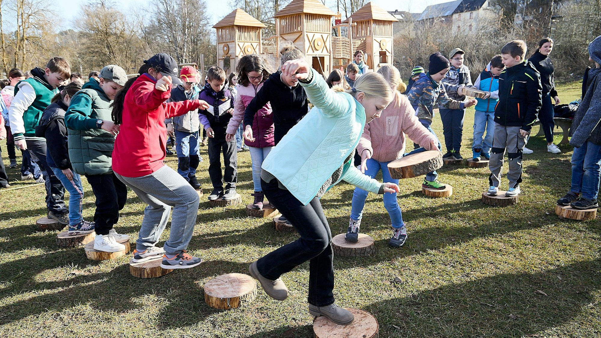 Kinder balancieren auf Holzscheiben, die auf einem Parcours ausgelegt sind. Im Hintergrund ist ein römisches Kastell zu sehen.