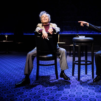 Helen Schneider (links) und Lucca Züchner sitzen auf Caféhausstühlen auf der Bühne der Stage 5 der New World Stages in New York. Schneider als Leonard Bernstein wirft lachend den Kopf zurück, Lucca Züchner als Herbert von Karajan, gestikuliert erregt mit dem Zeigefinger.
