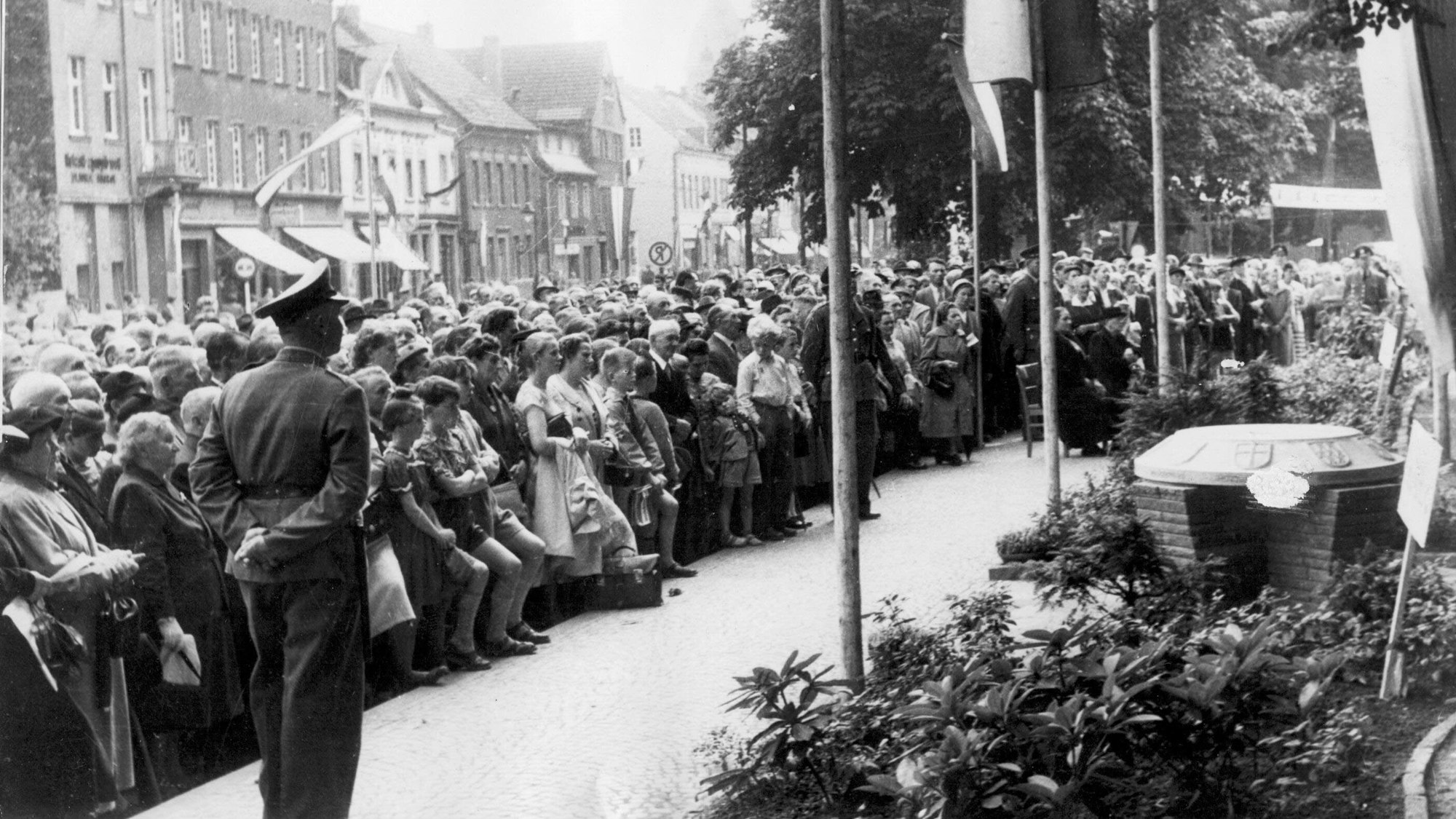 Historische Aufnahme von 1956: Viele Menschen stehen vor einem Gedenkstein. Auch ein Polizist.
