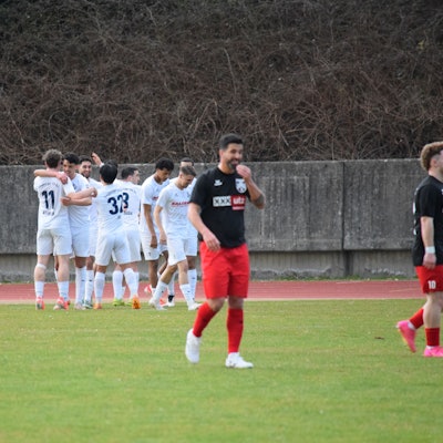 Die Siegburger bejubeln den Führungstreffer, Nils Teixeira vom FC Hennef 05 lächelt nur nach außen hin.