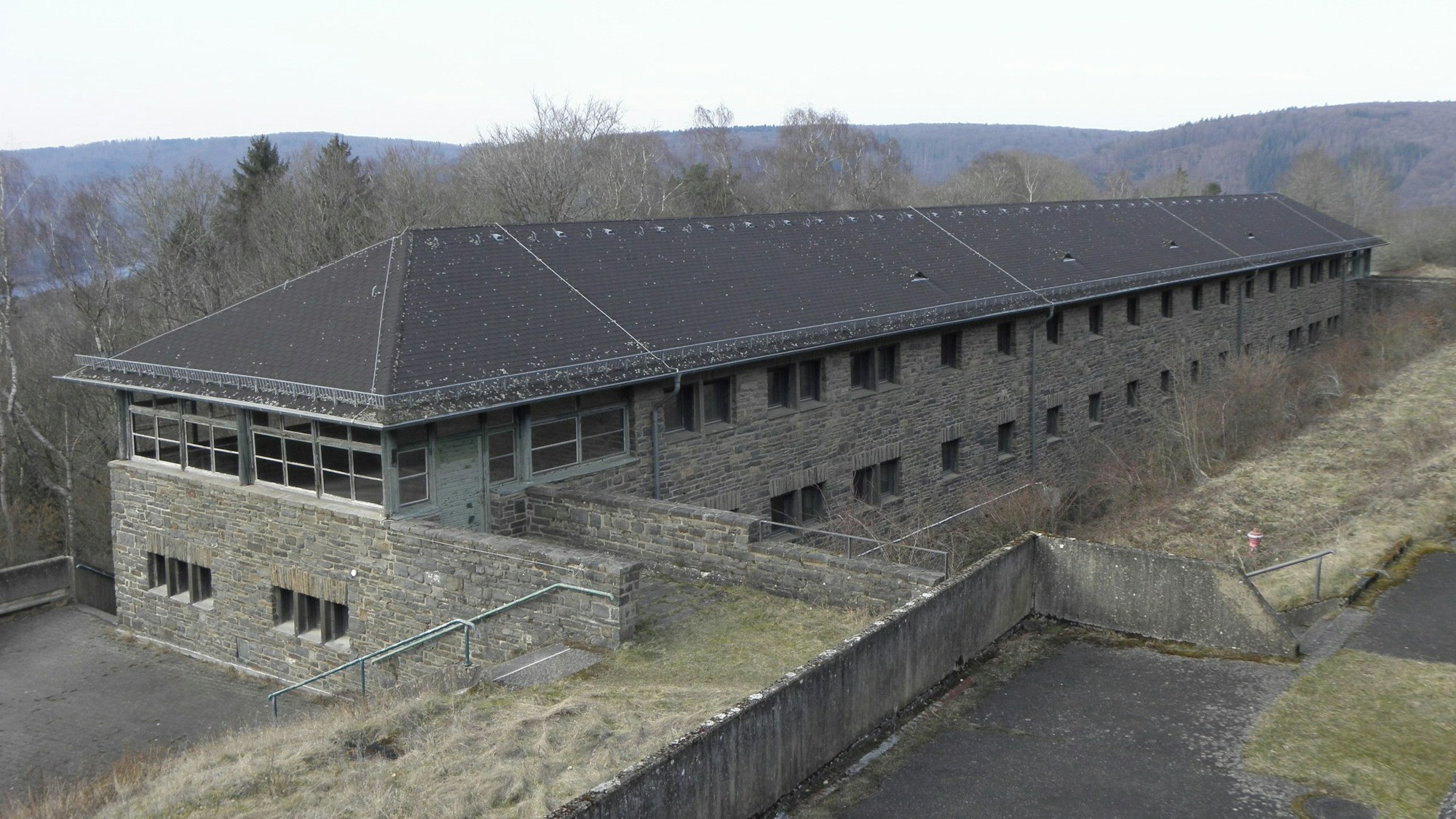 Der Blick auf eines der Hundertschaftshäuser, im Hintergrund sieht man ddie Waldkuppen des Nationalparks Eifel.