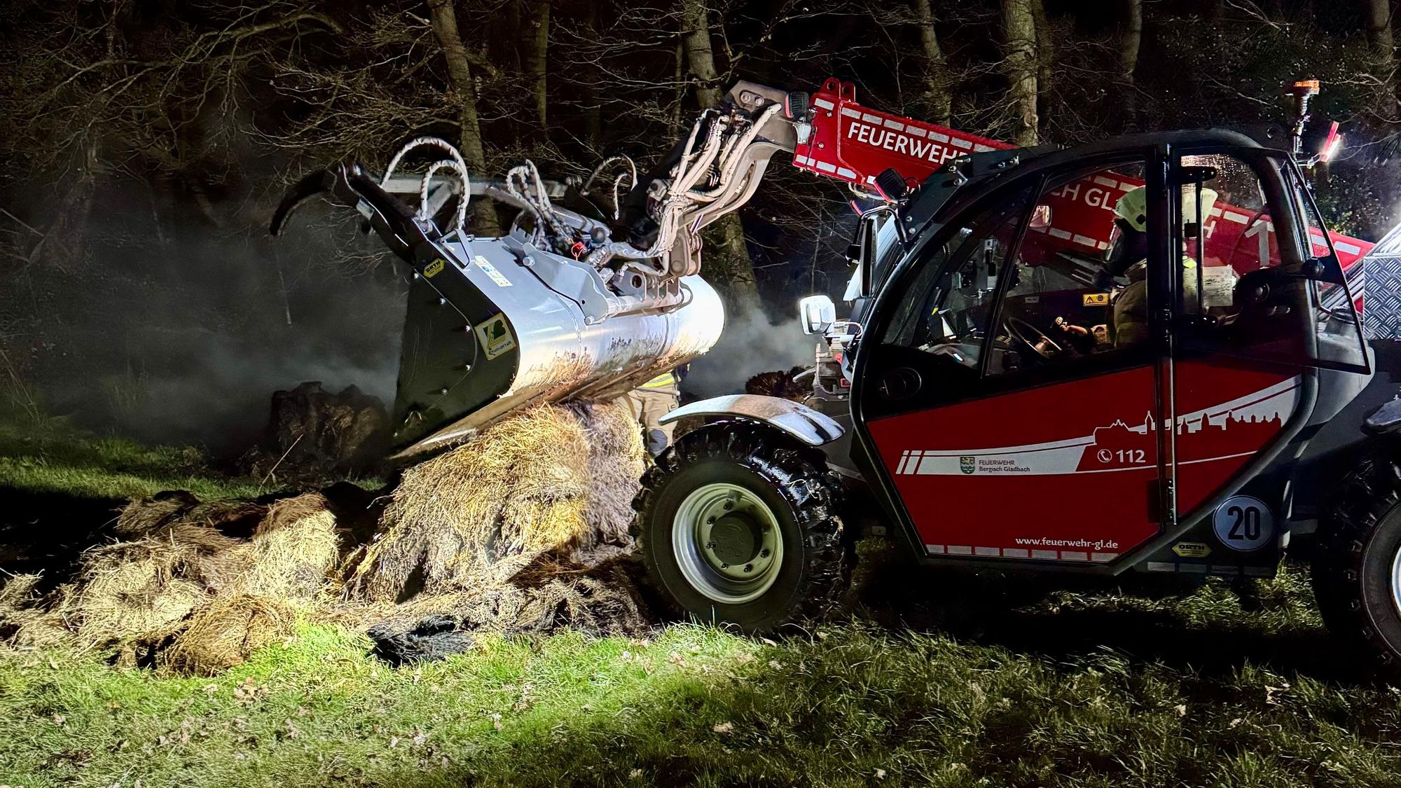 Ein Teleskoplader der Feuerwehr zieht qualmendes Heu auseinander.