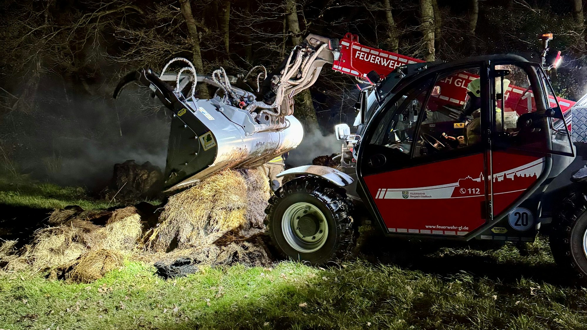 Ein Teleskoplader der Feuerwehr zieht qualmendes Heu auseinander.