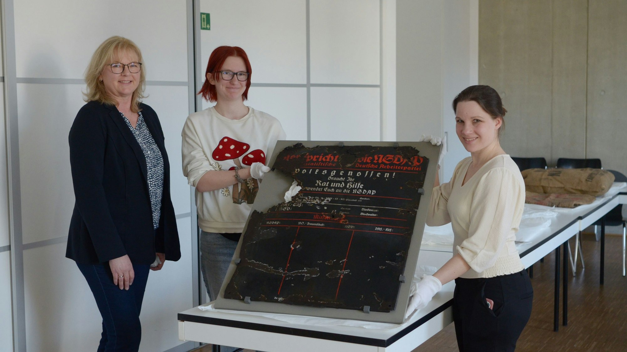 Das Foto zeigt die drei Frauen. Zwei von ihnen halten eine historische Infotafel.