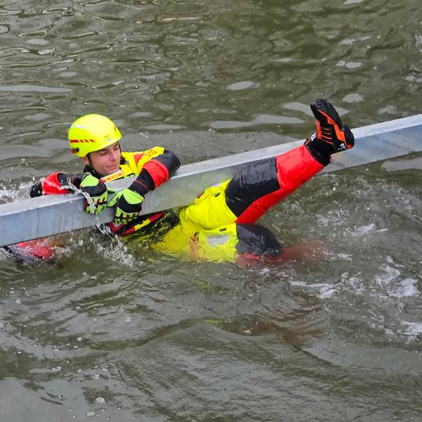 Zu sehen ist ein Strömungsretter der DLRG, der sich an einen Rettungsbalken im Wasser klammert.