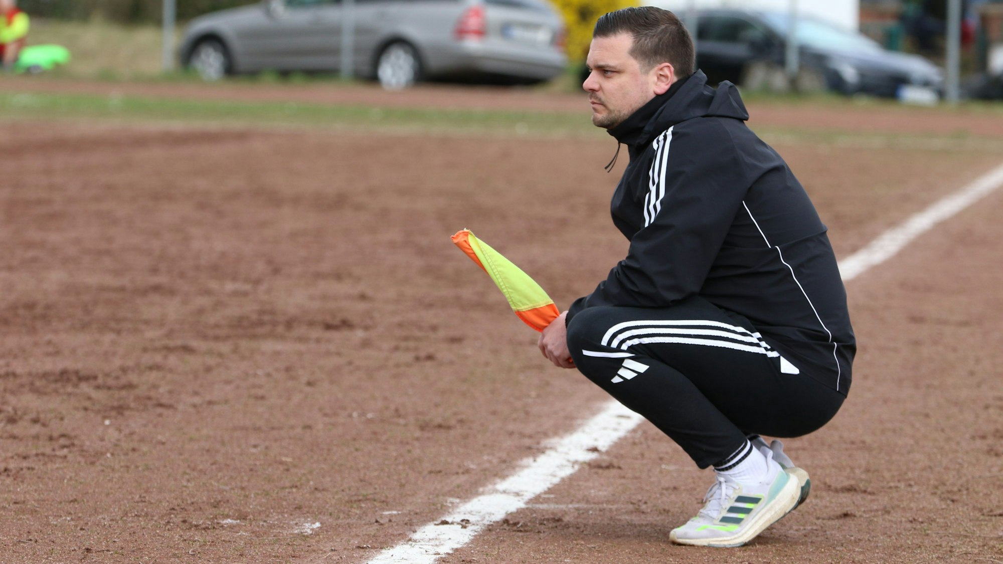 Der Trainer der Sportfreunde DHO hockt hinter der Seitenauslinie und hat eine Linienrichterfahne in der Hand.