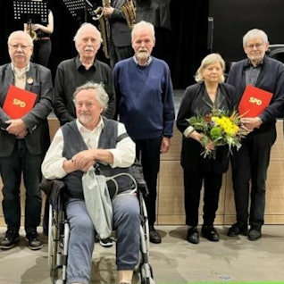 Zu sehen ist Willi Mengel, der im Rollstuhl sitzt. Hinter ihm stehen Parteifreunde.