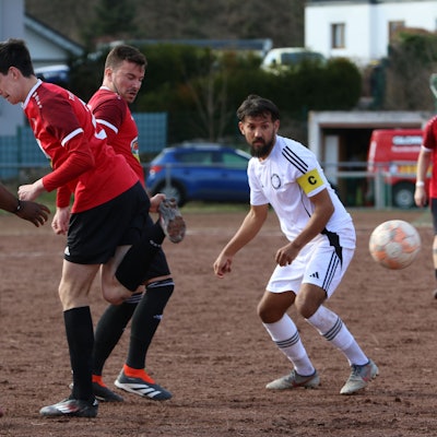 Mit der Hacke spielt ein Spieler den Ball. Mitspieler und Gegenspieler schauen überrascht.