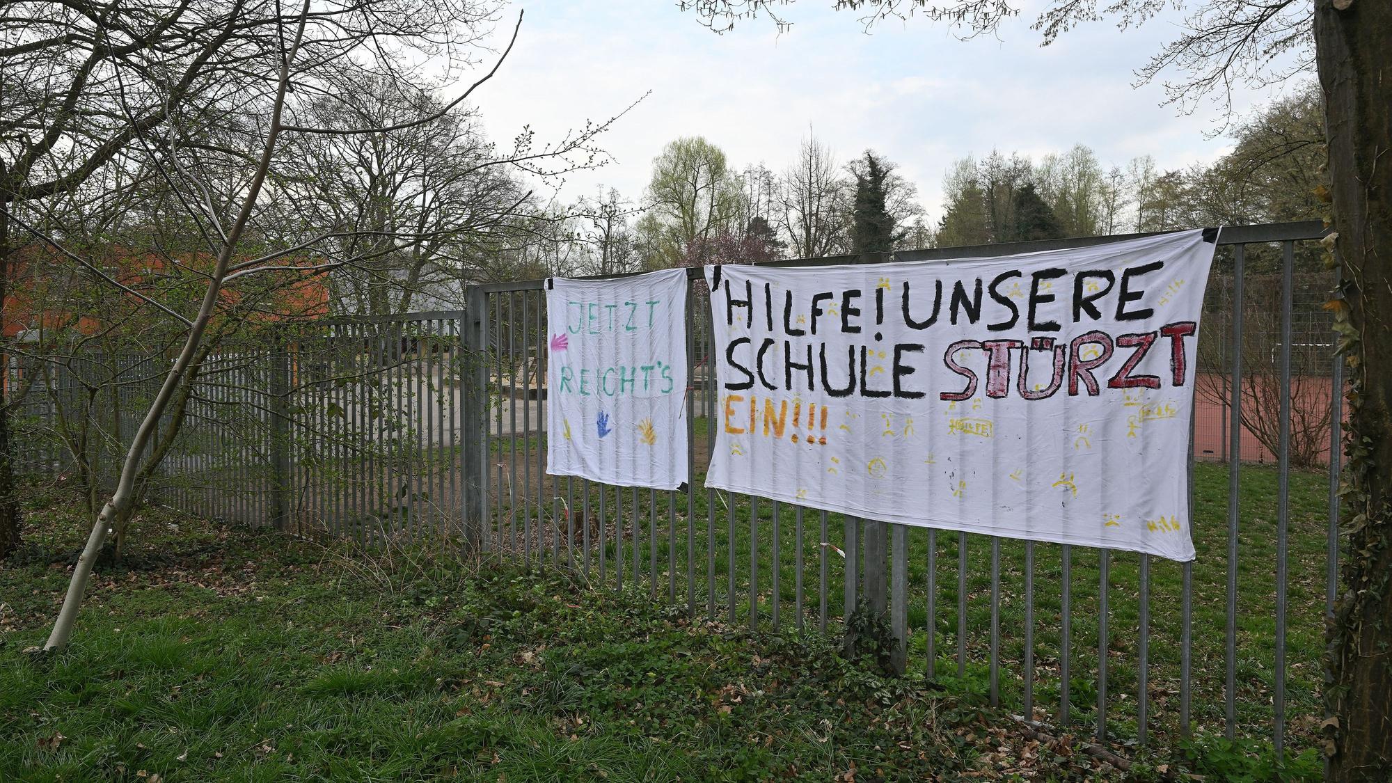 Zwei Plakate hängen an einem Zaun.