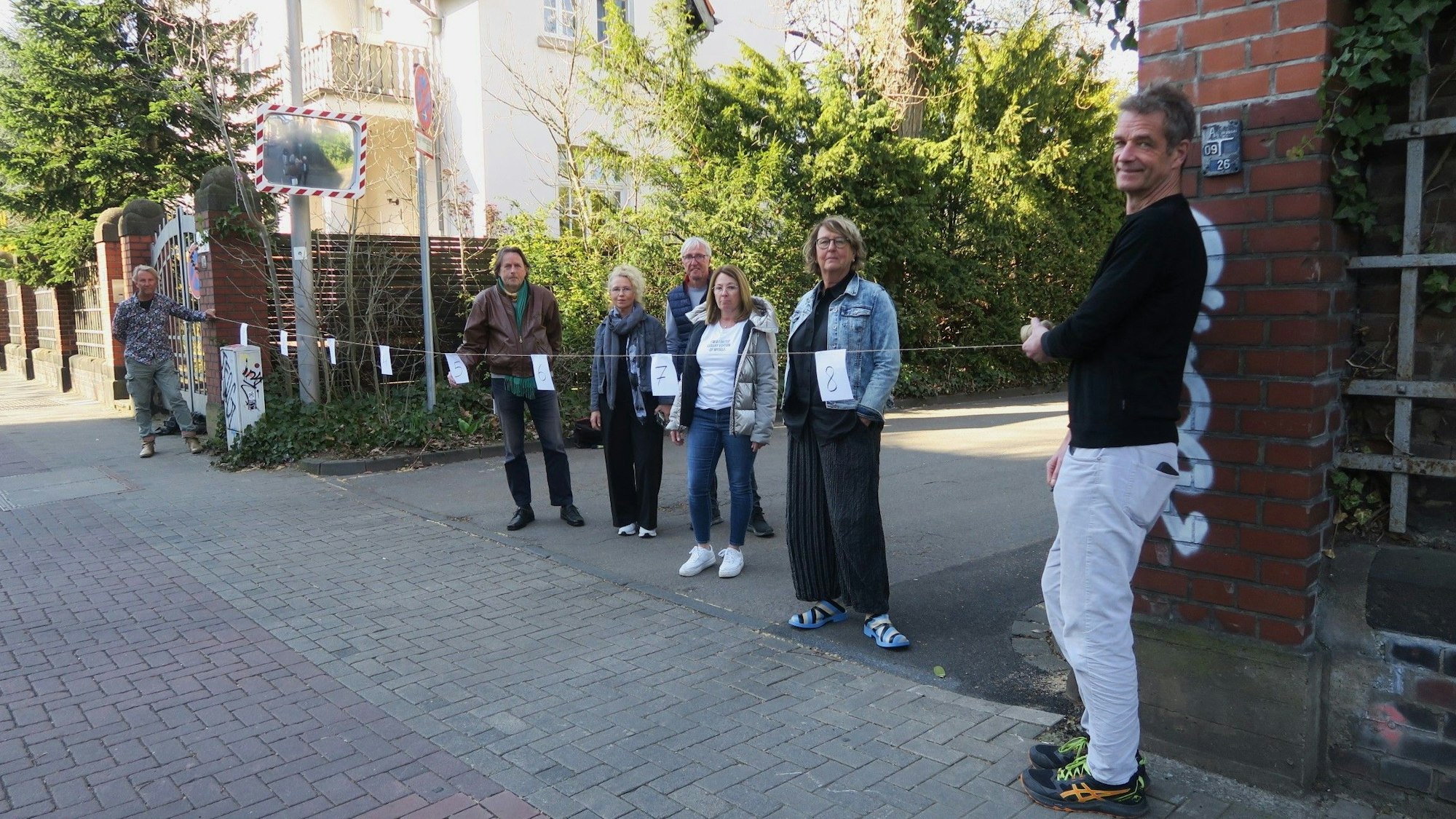 Sieben Personen halten ein 9 Meter langes Maßband von einer Hauswand zur nächsten.