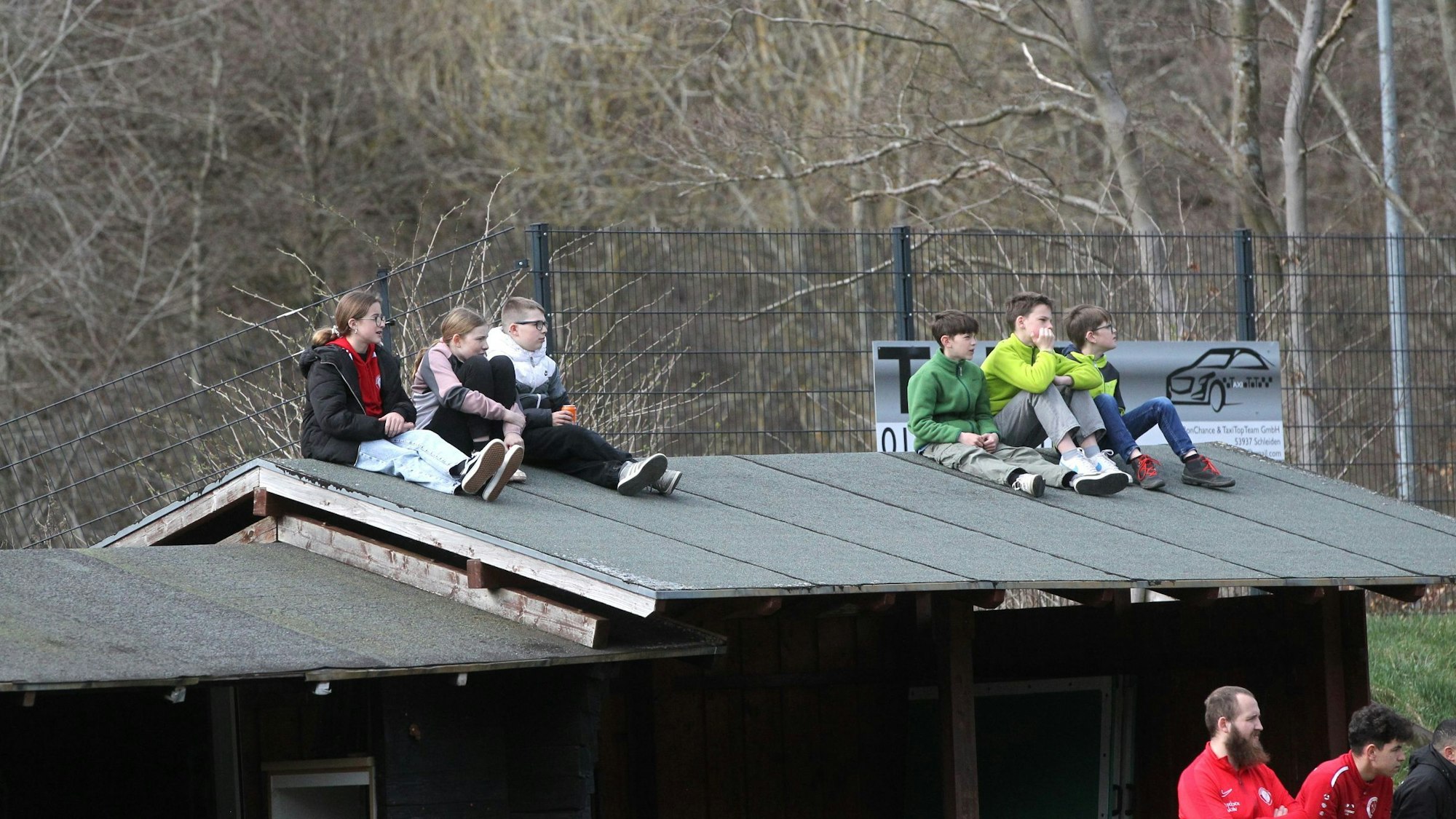 Sechs Kinder sitzen auf dem Dach und verfolgen ein Fußballspiel.