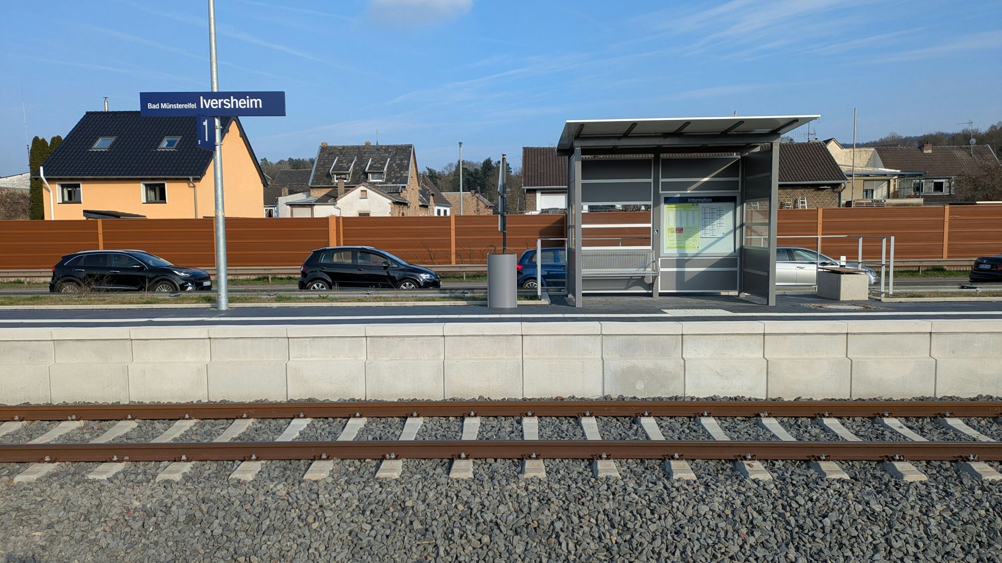 Das Bild zeigt einen Bahnsteig, auf dem sich ein Wartehäuschen, eine Bank und ein Mülleimer befinden.