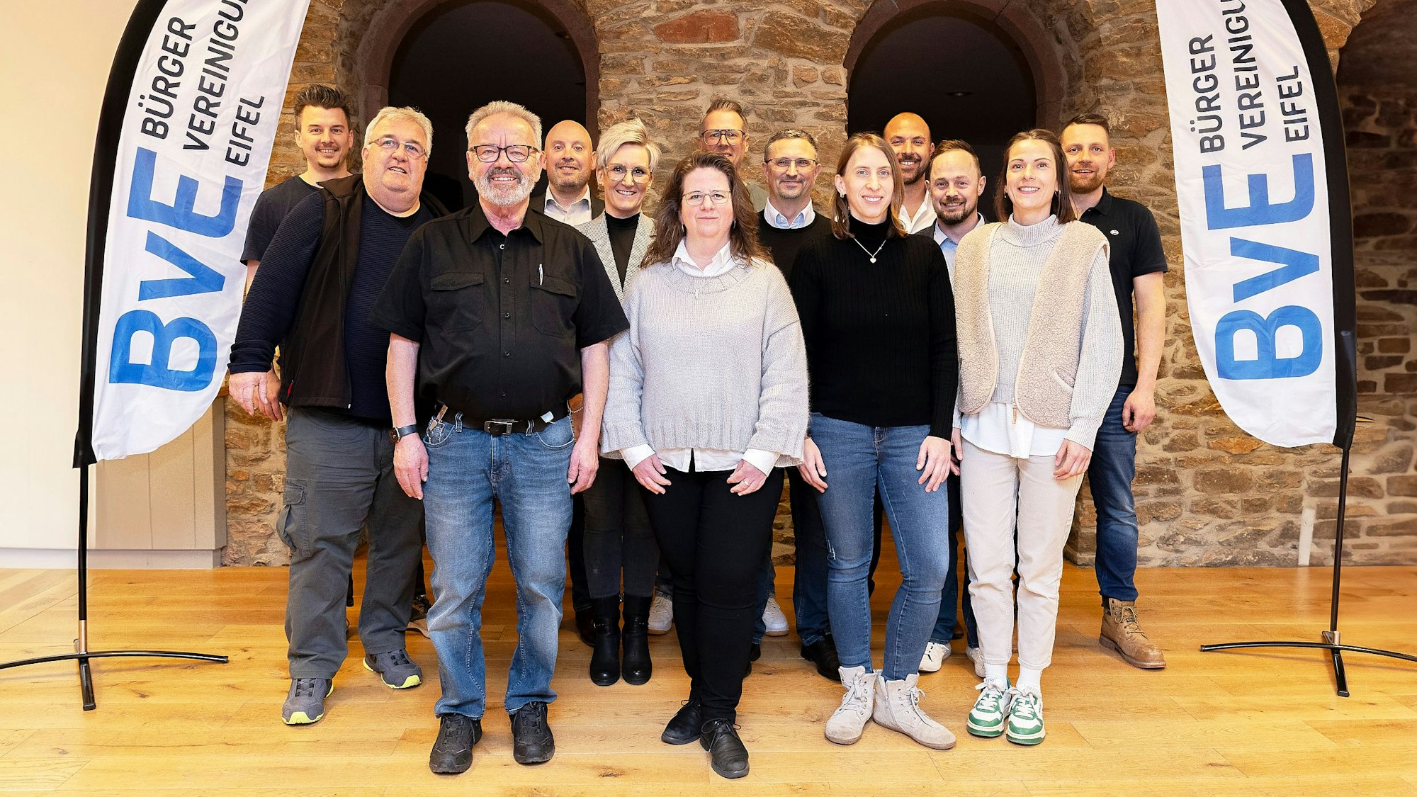 Eine Gruppe von Menschen steht zwischen zwei Fahnen, auf denen in blauen Buchstaben „BvE“ steht.