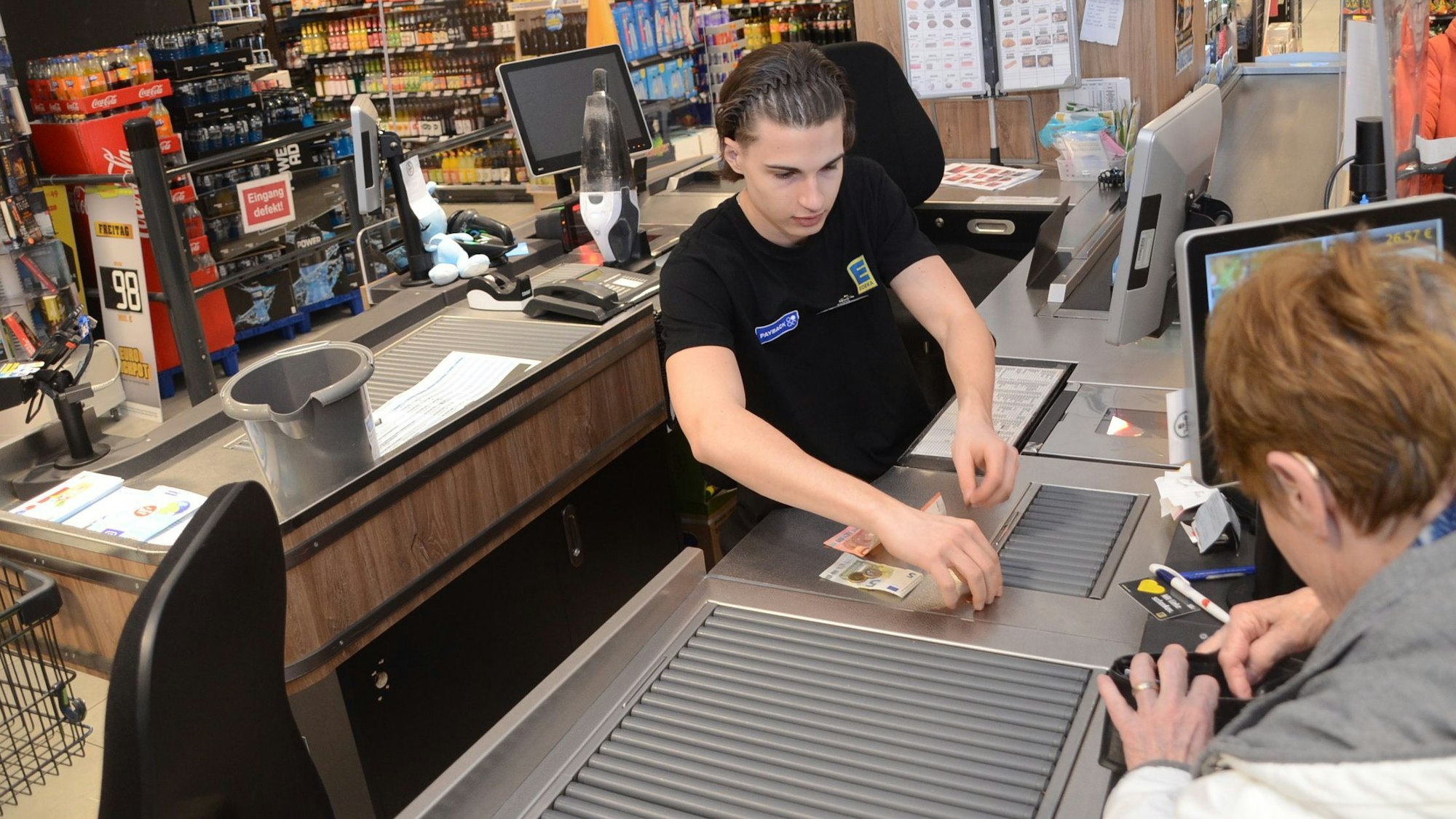 Ein junger Mann bedient eine Kundin an einer Supermarktkasse.