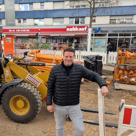 Das Foto zeigt den Nahkauf-Inhaber vor einem Radlader auf der Baustelle vor seinem Geschäft.