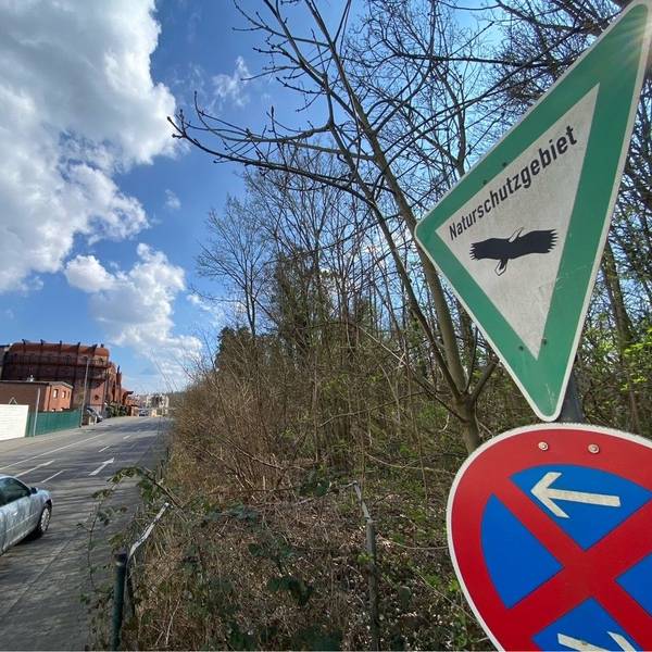 Zu sehen ist ein Schild, das auf das Naturschutzgebiet hinweist. Im Hintergrund ist das zum Phantasialand gehörende Hotel Charles Lindbergh zu sehen.