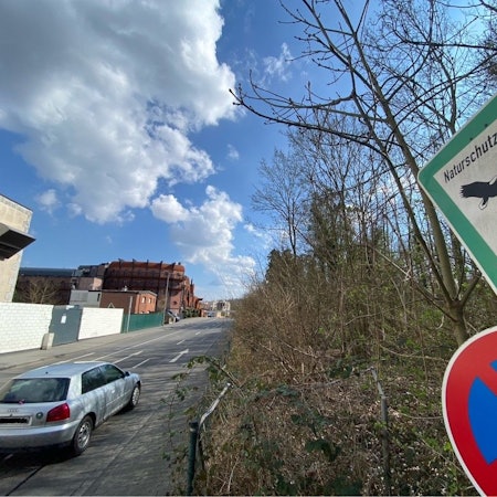 Zu sehen ist ein Schild, das auf das Naturschutzgebiet hinweist. Im Hintergrund ist das zum Phantasialand gehörende Hotel Charles Lindbergh zu sehen.
