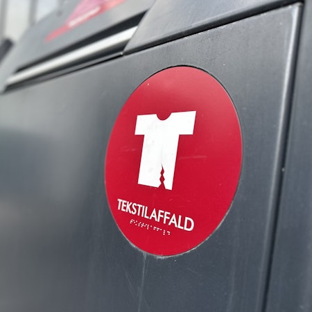 Eine Mülltonne für Textilabfall steht in Kopenhagen vor einem Einkaufszentrum.