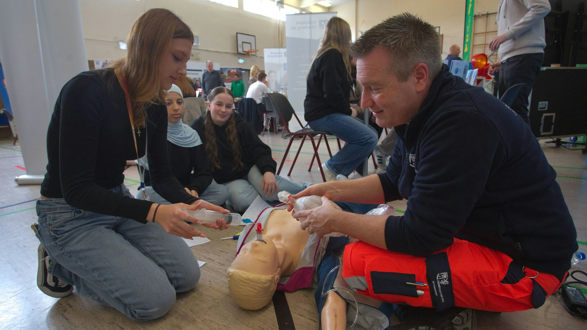 Ein Notfallsanitäter zeigt einer Schülerin an einer Trainingspuppe, wie eine Herz-Lungen-Massage funktioniert.