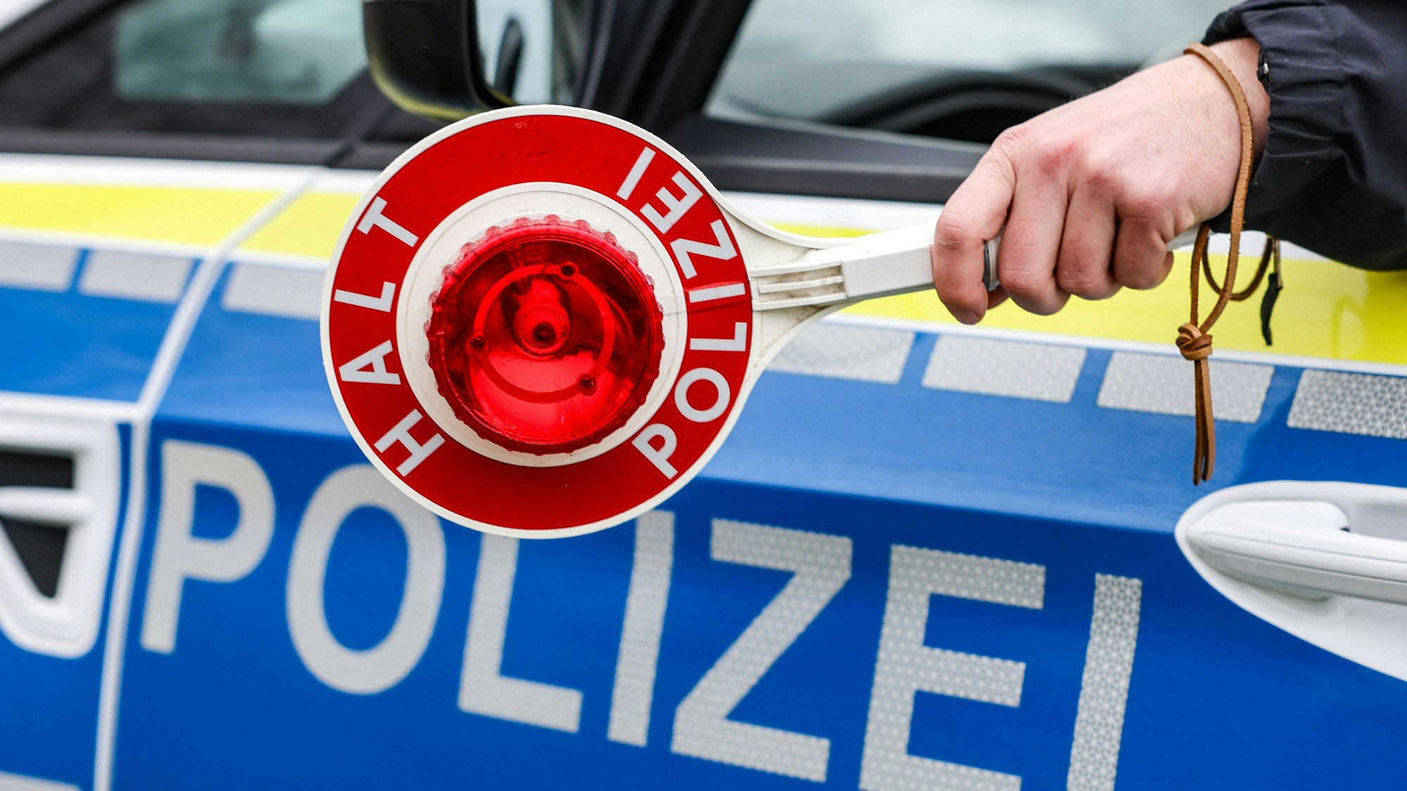 Ein Polizist hält eine Polizeikelle für eine Kontrolle aus dem Polizeiauto.