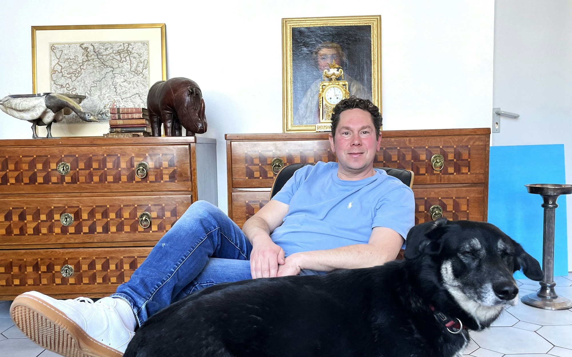 Ein Mann sitzt im Sessel, vor ihm steht ein Hund.