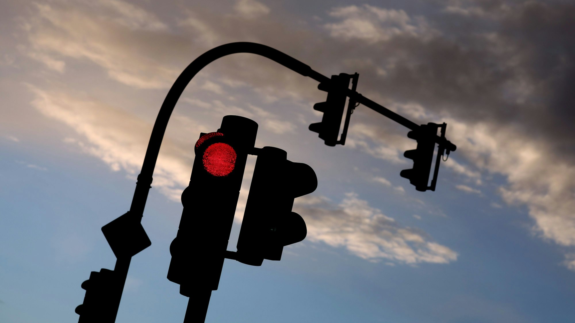 Eine auf Rot stehende Ampel leuchtet vor teilweise bewölktem Himmel. (Symbolbild)