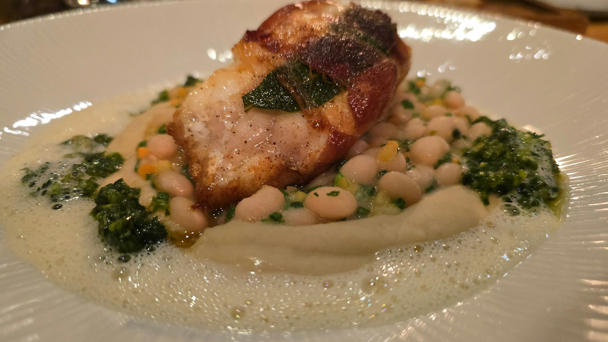 Tellergericht mit Fisch auf weißen Bohnen und gekräutertem Schaum
