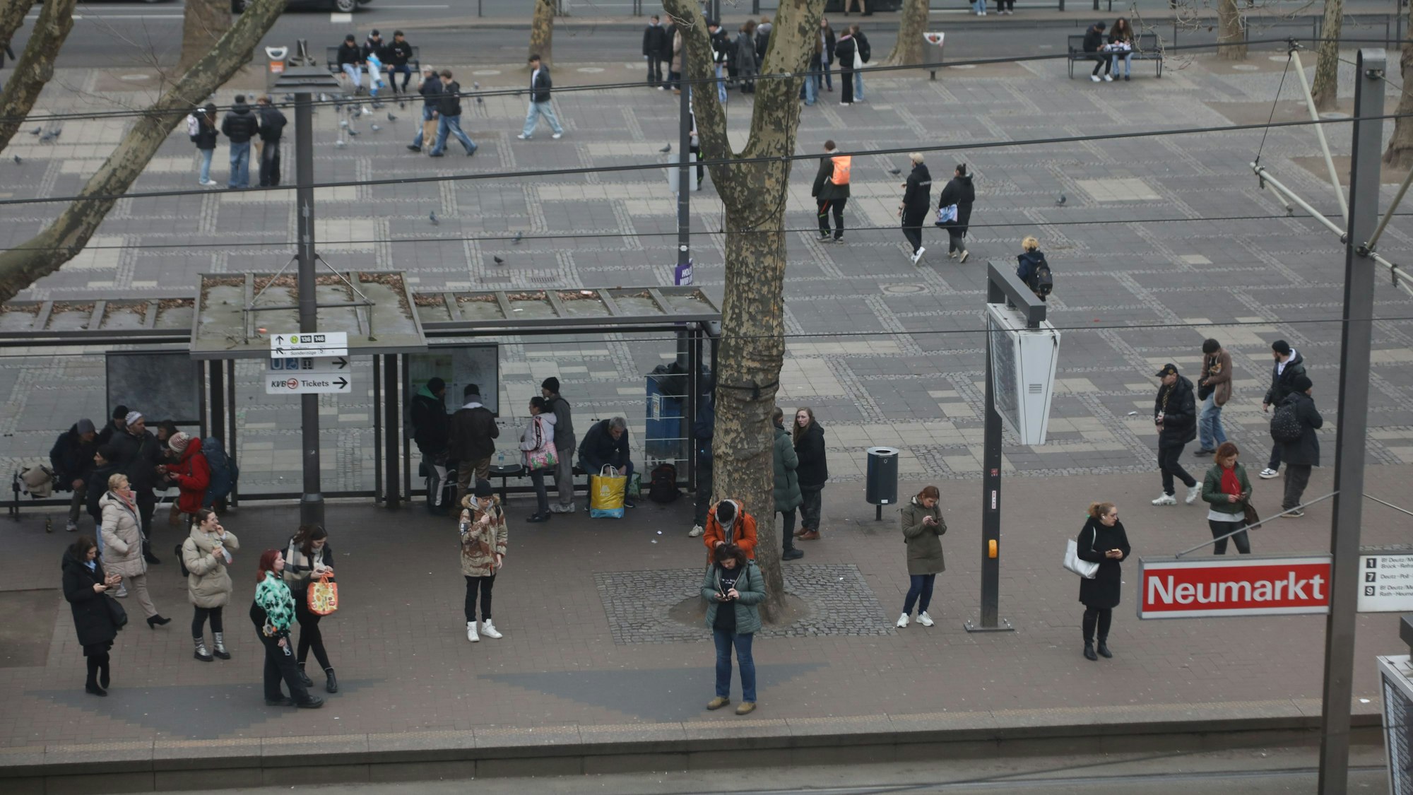 Verschiedene Menschen stehen an einer Bahn-Haltestelle am Neumarkt.