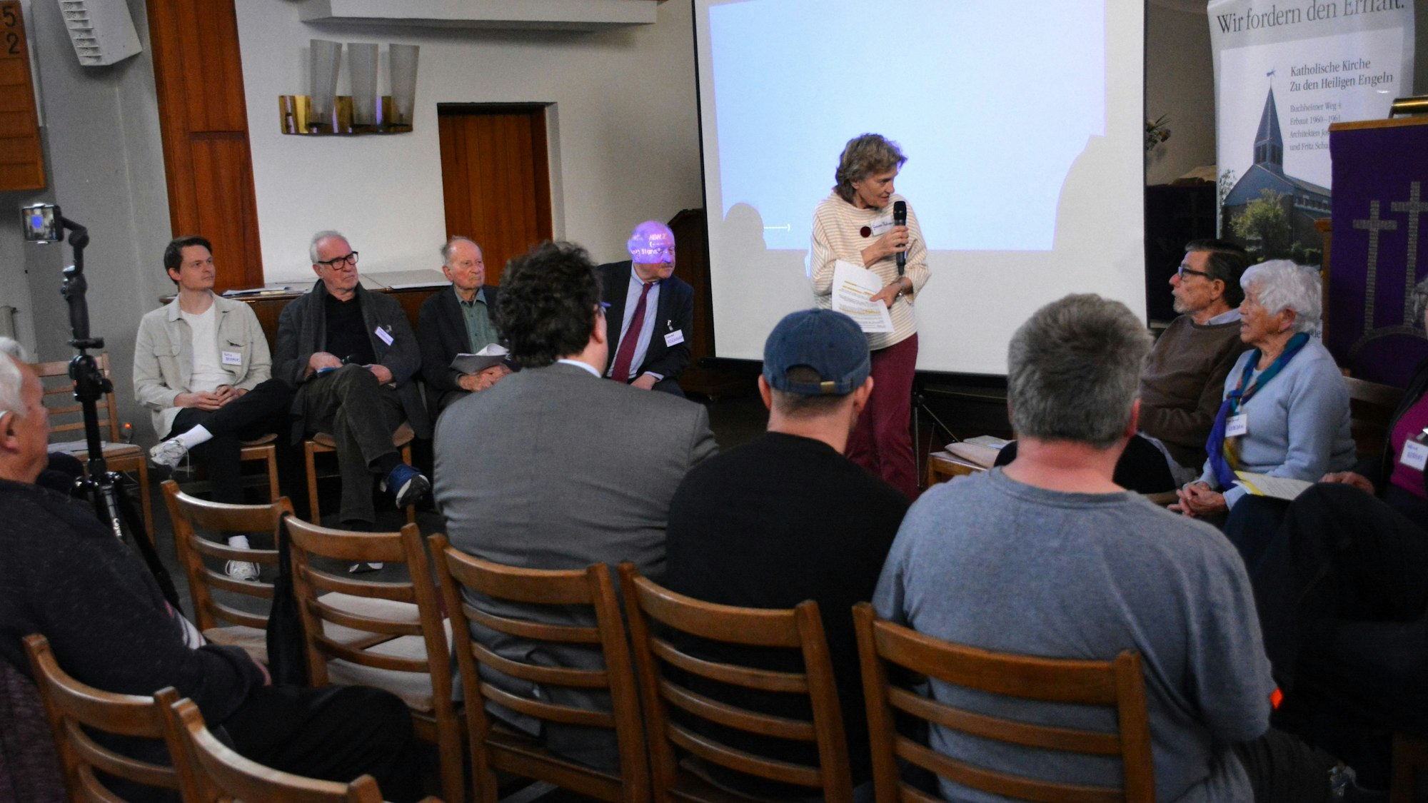 Eine Frau mit Mikrofon spricht mit Menschen, die auf Stühlen sitzen.