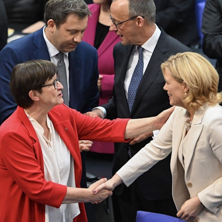 Julia Klöckner (rechts, CDU) erhält Glückwünsche von Saskia Esken (SPD), während sich im Hintergrund Friedrich Merz (rechts, CDU) und Lars Klingbeil (SPD) unterhalten.