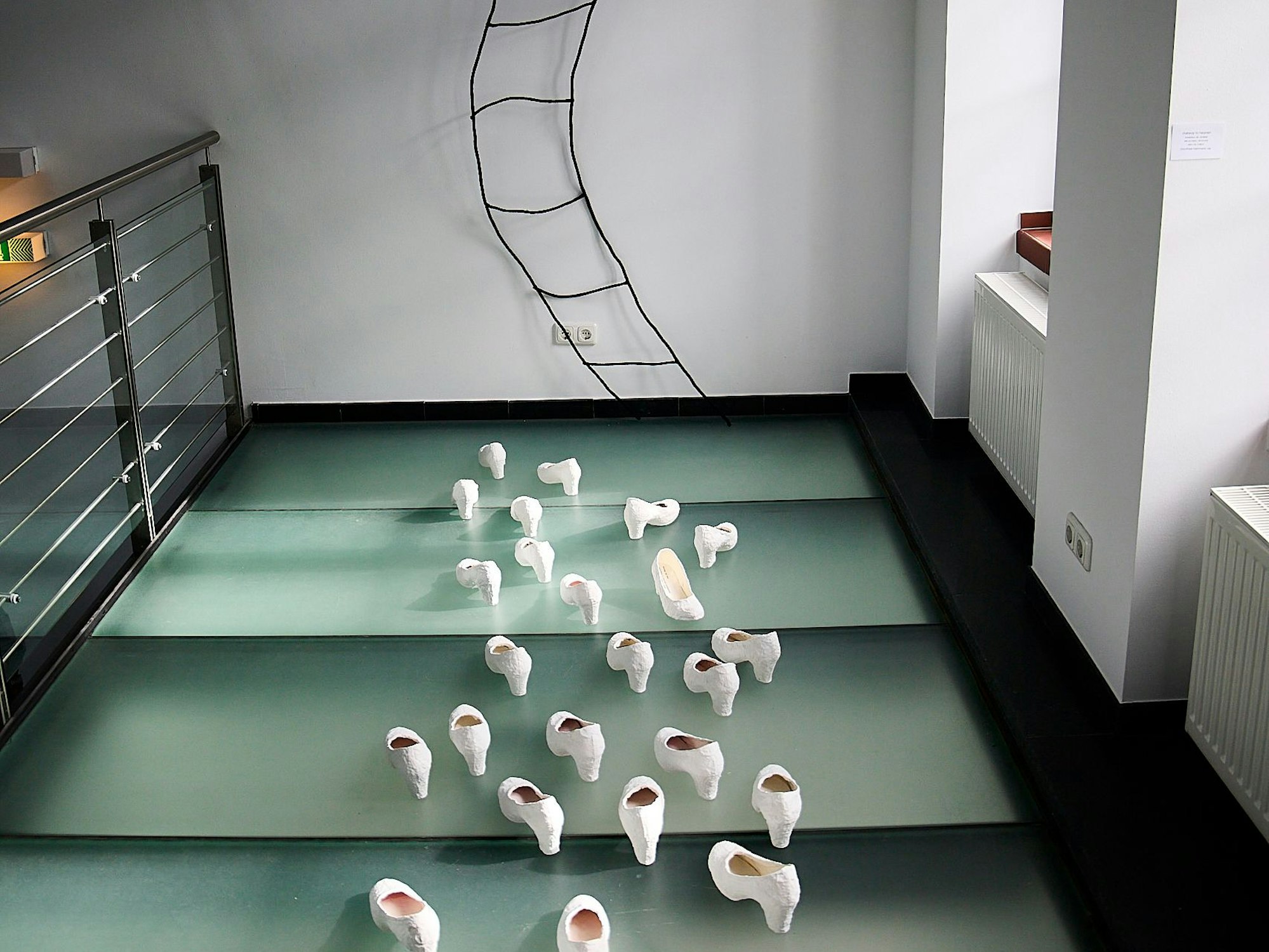 In der Kunst-Installation „Stairway to heaven“ von Dorothee Hermann sind weiße Pumps zu sehen. Sie sind auf eine Wand ausgerichtet, an der eine geschwungene Leiter nach oben führt.
