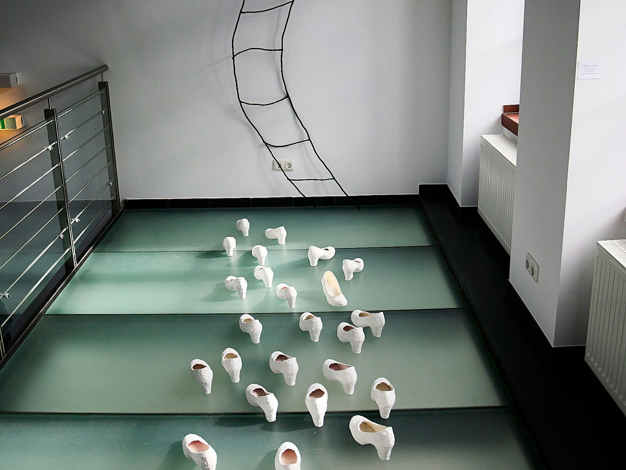 In der Kunst-Installation „Stairway to heaven“ von Dorothee Hermann sind weiße Pumps zu sehen. Sie sind auf eine Wand ausgerichtet, an der eine geschwungene Leiter nach oben führt.