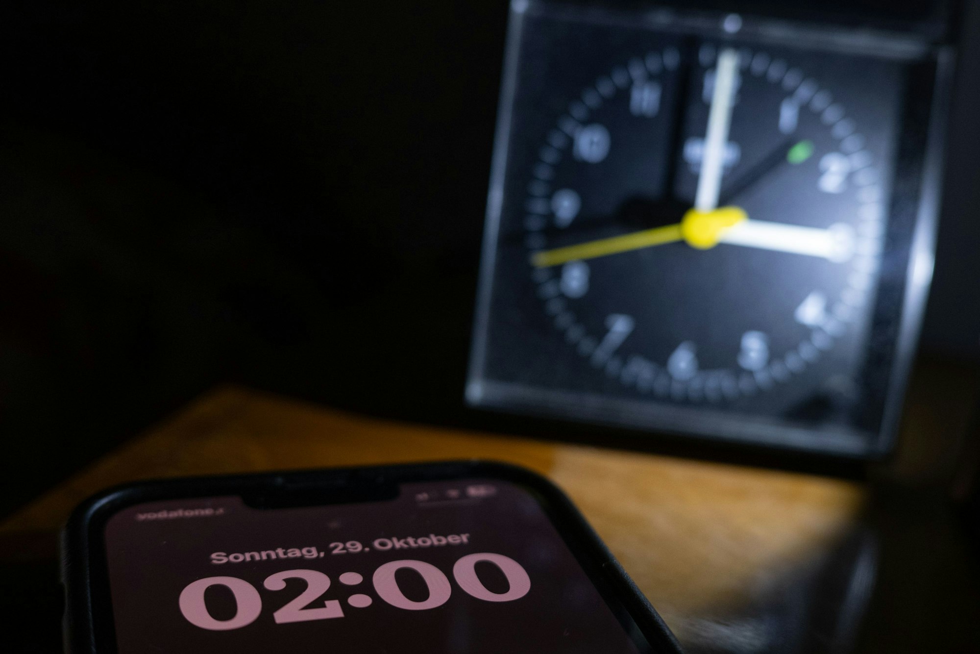 Ein Smartphone, auf dem "02:00" steht, liegt auf einem Nachttisch vor einem Wecker, der drei Uhr anzeigt.
Viele Uhren stellen sich automatisch um.
