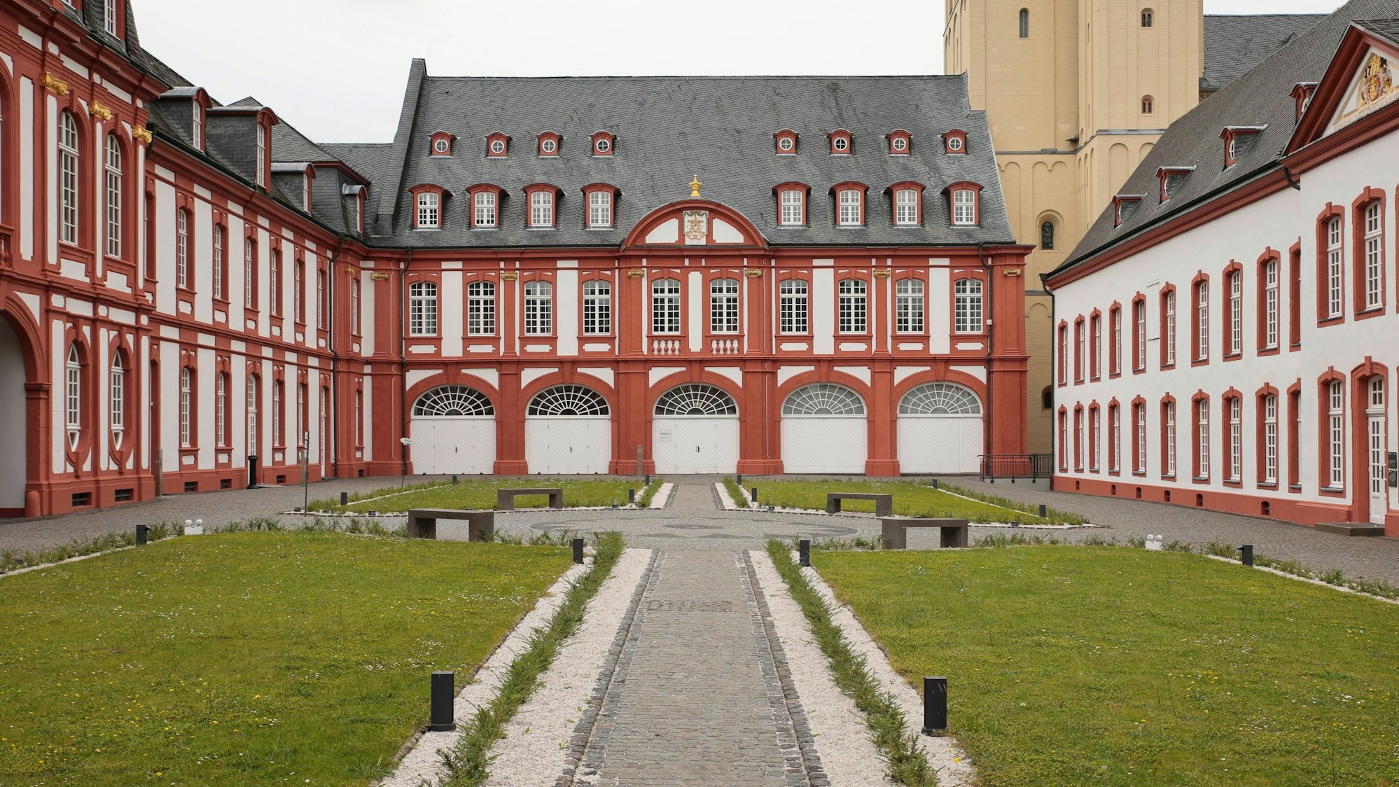 Die rot-weißen Gebäude der Abtei Brauweiler umringen einen bepflanzten Innenhof.