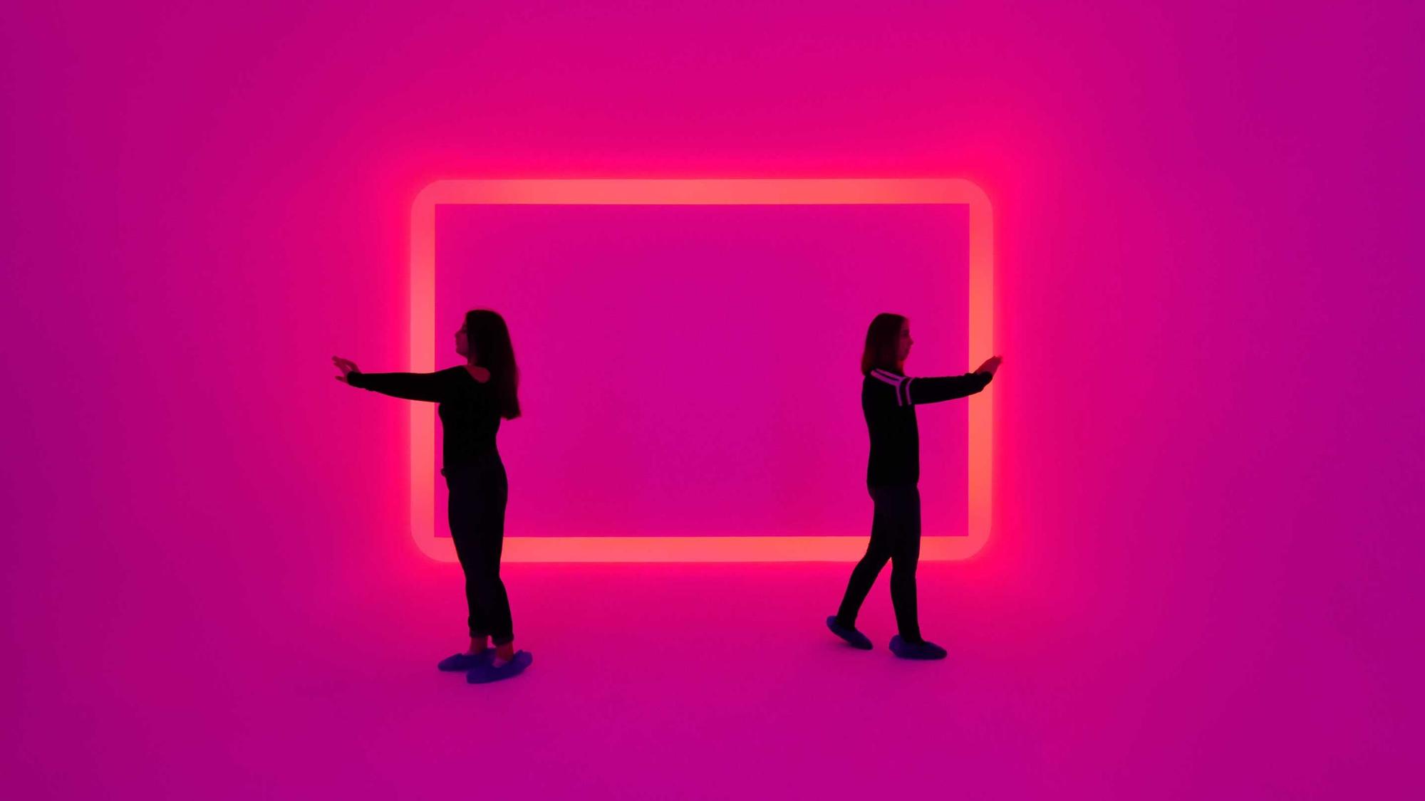 Zwei Frauen stehen in einem Raum, der in pink leuchtet.