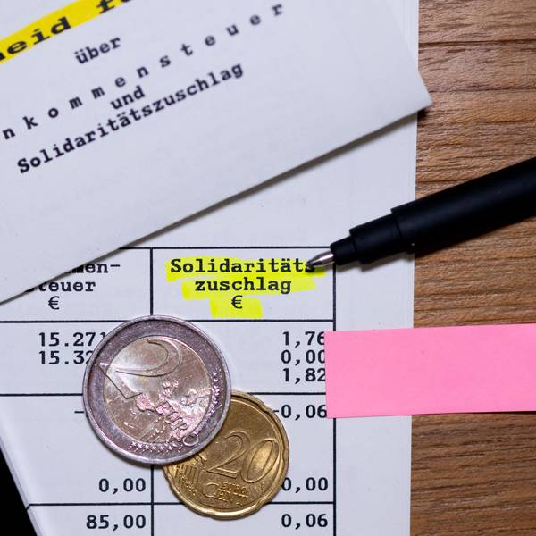 Das Wort „Solidaritätszuschlag“ ist neben einem Taschenrechner und einem Stift auf einem Steuerbescheid zu sehen. (Symbolbild)