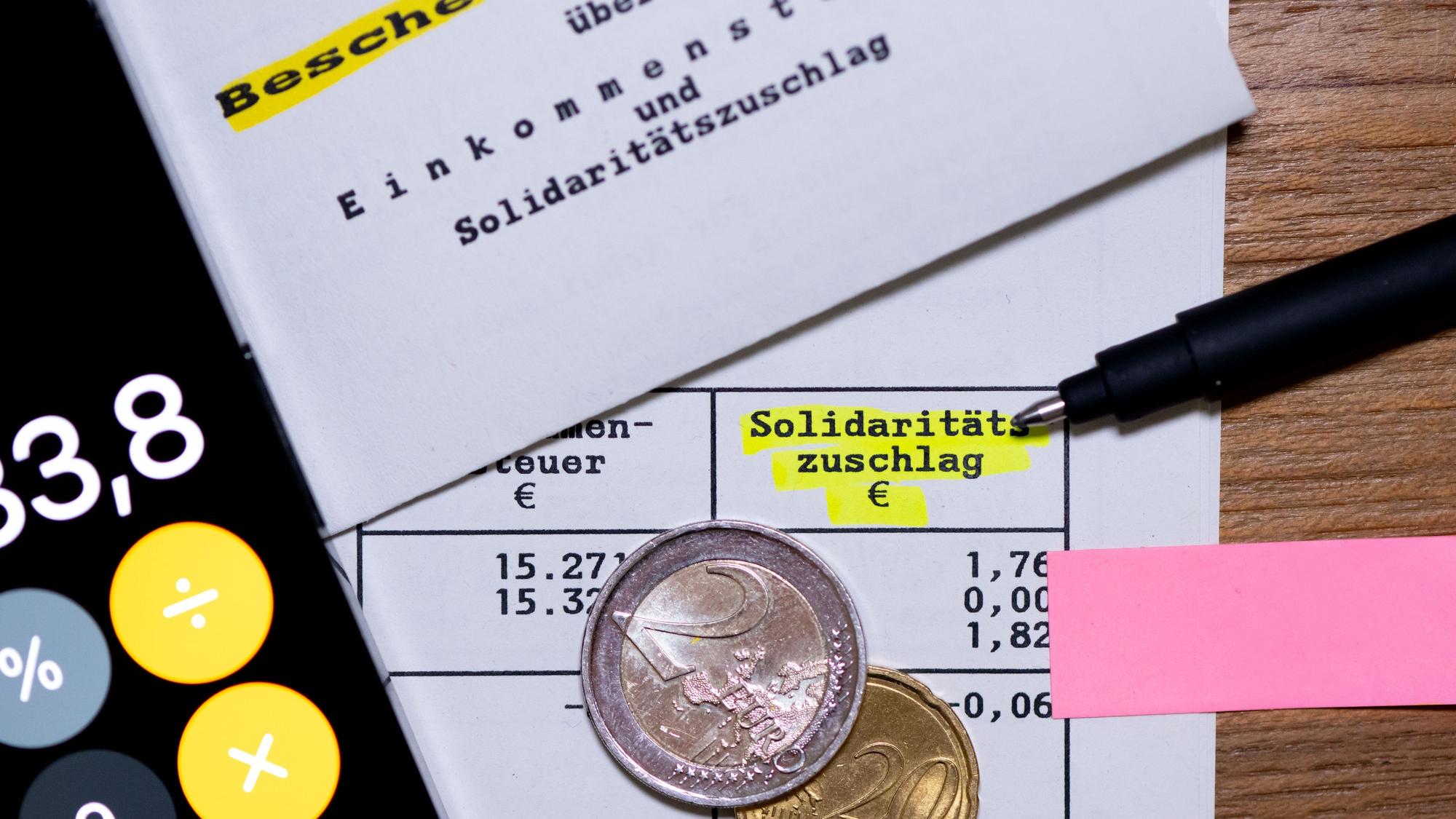 Das Wort „Solidaritätszuschlag“ ist neben einem Taschenrechner und einem Stift auf einem Steuerbescheid zu sehen. (Symbolbild)