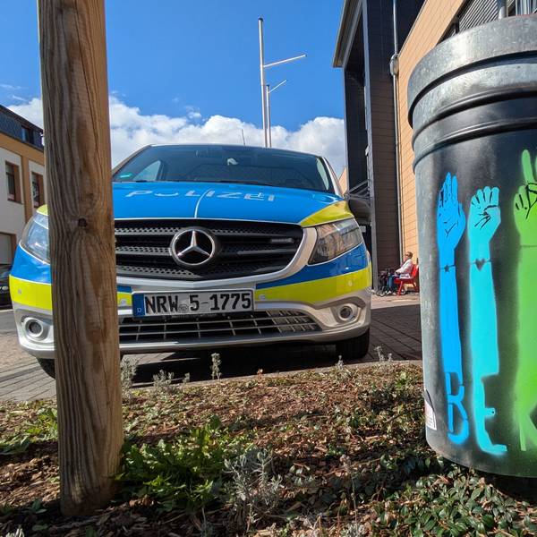Der englischsprachige Schriftzug „Be kind“ ist auf einer in verschiedenen Farben besprühten Mülltonne zu lesen. Links steht ein Einsatzfahrzeug der Polizei.